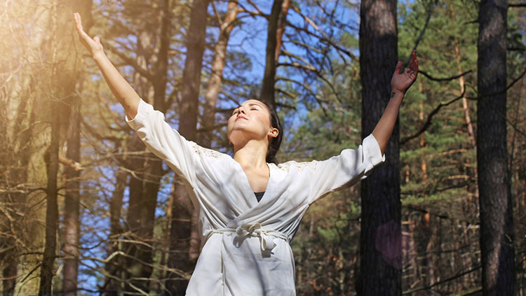 Woman in white wrap top forest bathing (Shinrin yoku), in wooded area